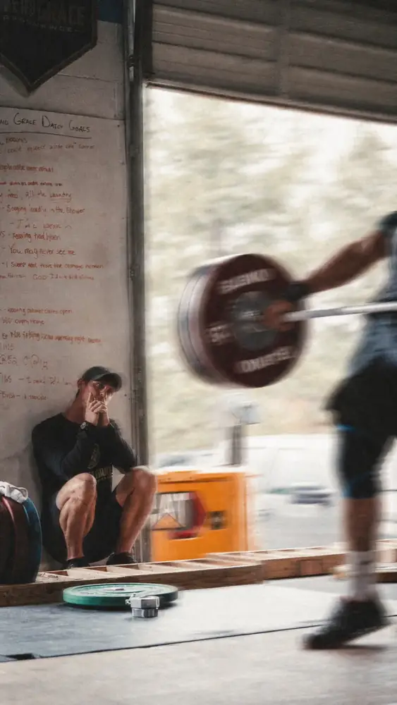 Athlete lifting an Olympic barbell while a coach watches